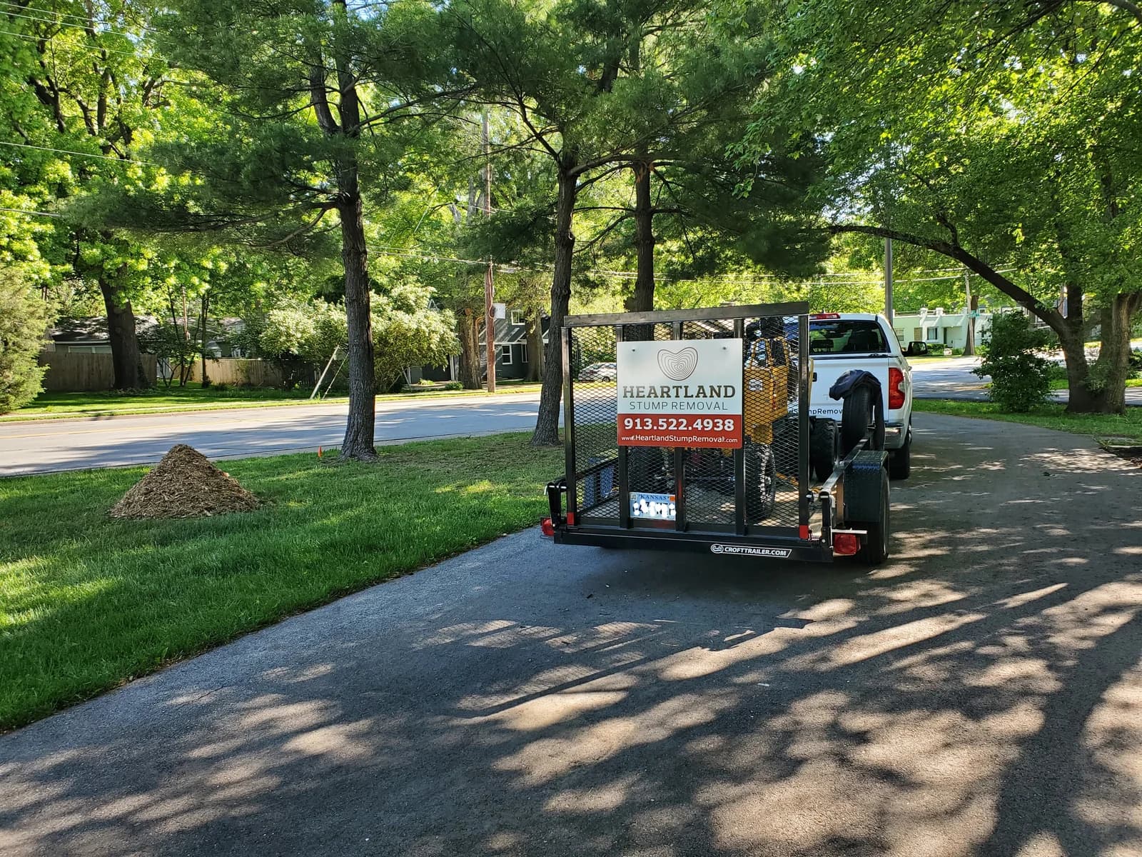 Heartland’s truck and branded trailer beside a lawn with a neat pile of stump grindings